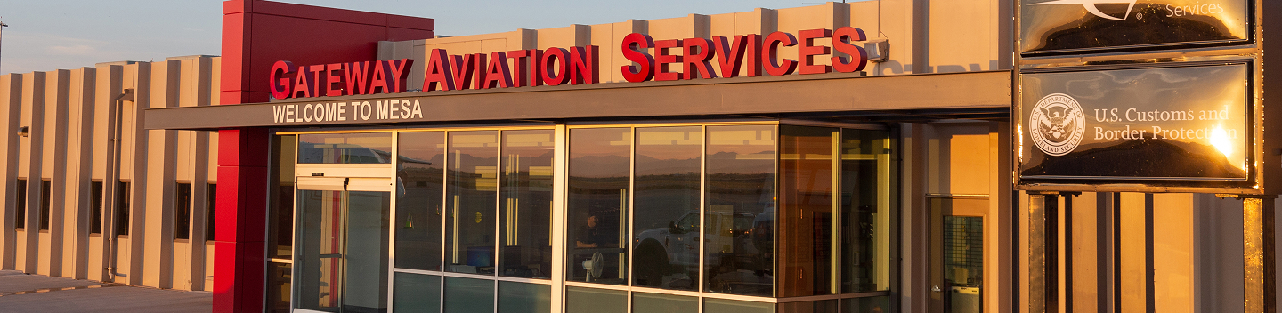 Exterior view of the Gateway Aviation Services building at sunset, with large red letters and reflective glass windows. A sign for U.S. Customs and Border Protection is also visible.